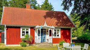 A red house with a white porch and a blue door, surrounded by a well-maintained lawn and trees.