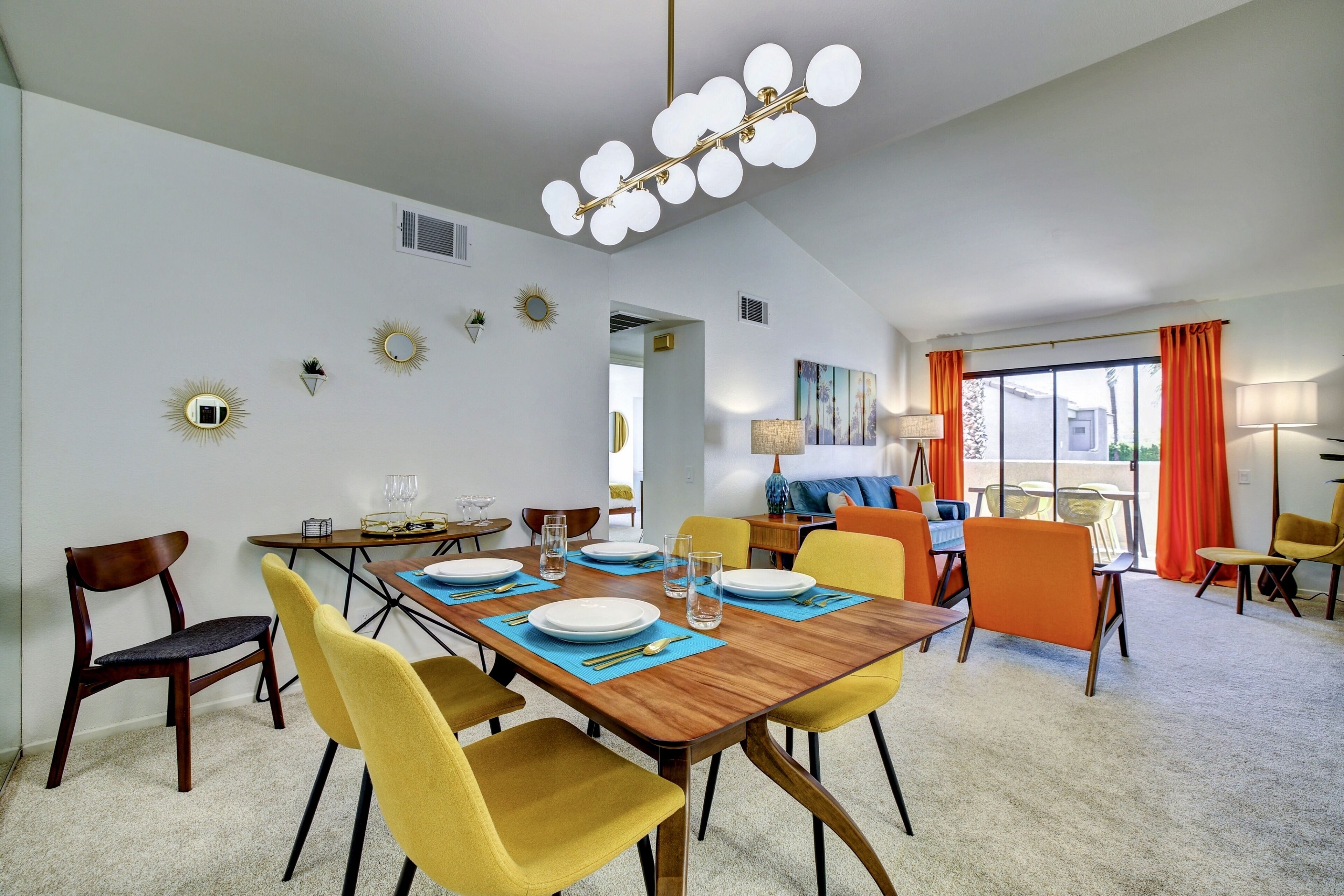 Un coin repas avec une table en bois dressée pour quatre personnes, des chaises jaunes et un lustre moderne.