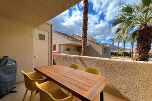 A wooden table with yellow chairs in a covered outdoor area with a view of a mountain and palm trees. - Mid Century Escape. Envious location. (Palm Springs)