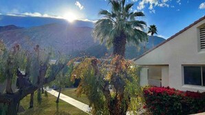 Un barrio residencial con una palmera, una casa con ventana y montañas al fondo.