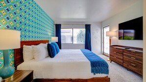 Un dormitorio ordenado con cama, mesitas de noche, cómoda y televisor en la pared.