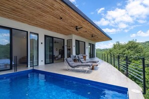A modern house with a swimming pool, outdoor seating, and a view of the surrounding landscape.