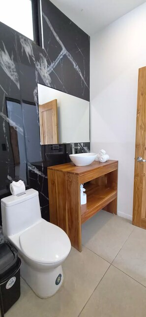 Et badeværelse med toilet, vask, spejl og en trækommode.