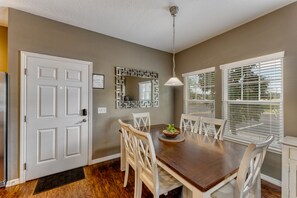 A dining area with a wooden table, white chairs, a decorative mirror, and a ceiling light. - Beautiful Town Home in Gated Community With Amenities - Close to WDW (Kissimmee)