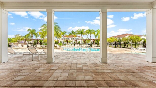 A covered outdoor area with a pool, lounge chairs, and a view of a residential neighborhood. - Beautiful Town Home in Gated Community With Amenities - Close to WDW (Kissimmee)