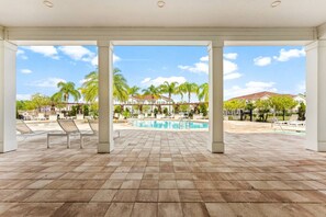 A covered outdoor area with a pool, lounge chairs, and a view of a residential neighborhood. - Beautiful Town Home in Gated Community With Amenities - Close to WDW (Kissimmee)