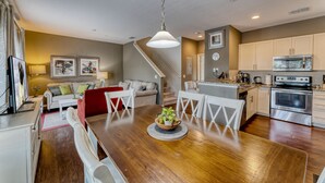 A modern kitchen with stainless steel appliances, a dining area with a wooden table and white chairs, and a staircase leading to another level. - Beautiful Town Home in Gated Community With Amenities - Close to WDW (Kissimmee)