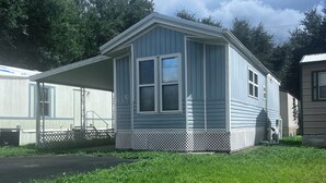 A small, single-story mobile home with a porch and a fenced yard. - Quaint and Quiet Tiny Home, with Pool Access! (Harlingen)