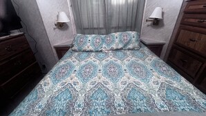 A bedroom with a patterned bedspread, two bedside lamps, a wooden dresser, and a television on a dresser. - Quaint and Quiet Tiny Home, with Pool Access! (Harlingen)