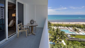 A balcony with a table and chairs, a view of the beach, and a pool area.