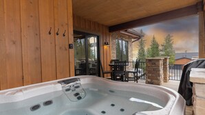 En træterrasse med jacuzzi, stensøjle og udendørs siddeområde med stole og borde.