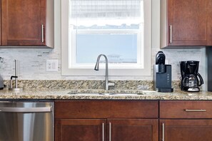 A kitchen with a granite countertop, stainless steel sink, and wooden cabinets. - TJs Beach Bungalow:Private & community pool, hot tub, dog friendly and elevator! (Corolla)