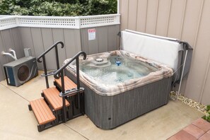 A spa hot tub with steps and a fan, set against a wooden fence.
