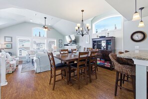 A spacious living area with a dining table, wooden chairs, a sofa, and a kitchen area with a dining table and chairs.