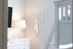 A white dresser with a lamp, a crib, and seahorse wall decor.