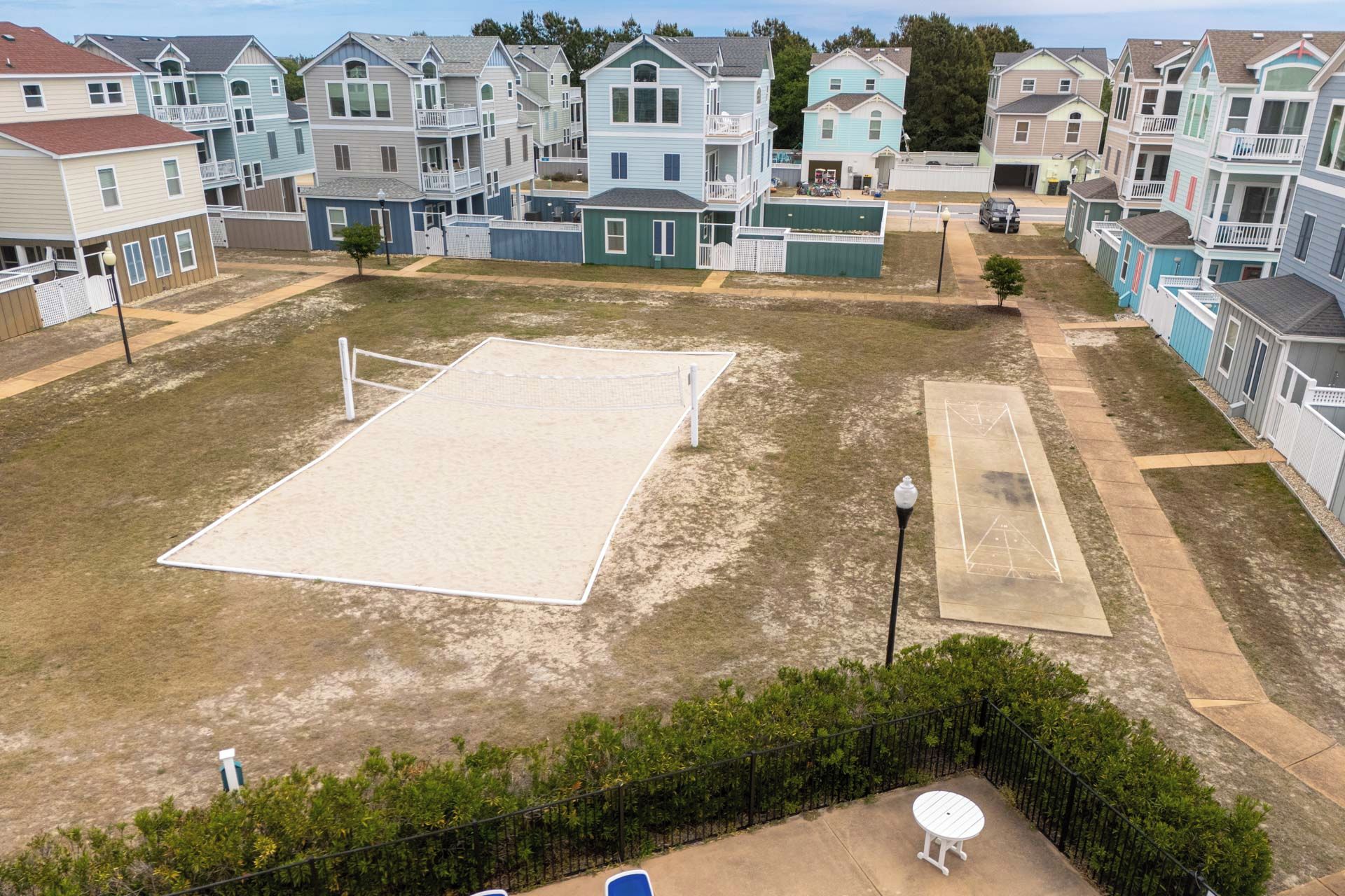 A residential area with multiple two-story houses, a volleyball court, and a small patio with a table and chairs.