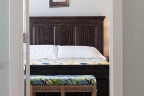 A bedroom with a wooden headboard, a bed with white linens, and a bench with a floral cushion.