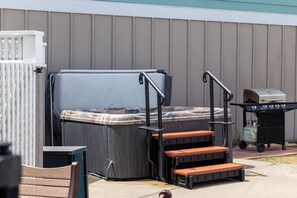 A hot tub with steps, a grill, and a covered pool.