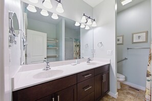 A bathroom with a double sink vanity, a large mirror, and a shower area.