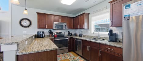 A kitchen with wooden cabinets, stainless steel appliances, a granite countertop, and a clock on the wall.
