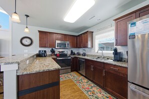 A kitchen with wooden cabinets, stainless steel appliances, a granite countertop, and a clock on the wall.