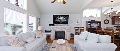 A spacious living room with a fireplace, two white sofas, a coffee table, and a ceiling fan.