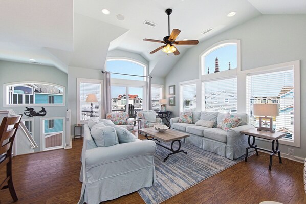 A spacious living room with a ceiling fan, large windows, and a view of the outside.
