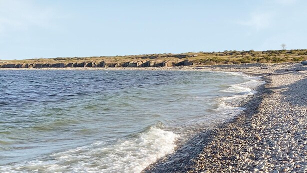 Pikkukivinen ranta, jossa on tyyni vesi ja kivikkoinen rantaviiva.
