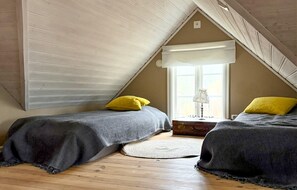 Ein Schlafzimmer mit zwei Betten, einem Fenster inklusive Lampe und Holzboden.