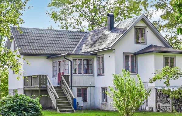 Ein zweistöckiges Haus mit einem steilen Satteldach, einem sichtbaren Schornstein und einer kleinen Treppe, die zum Obergeschoss führt.