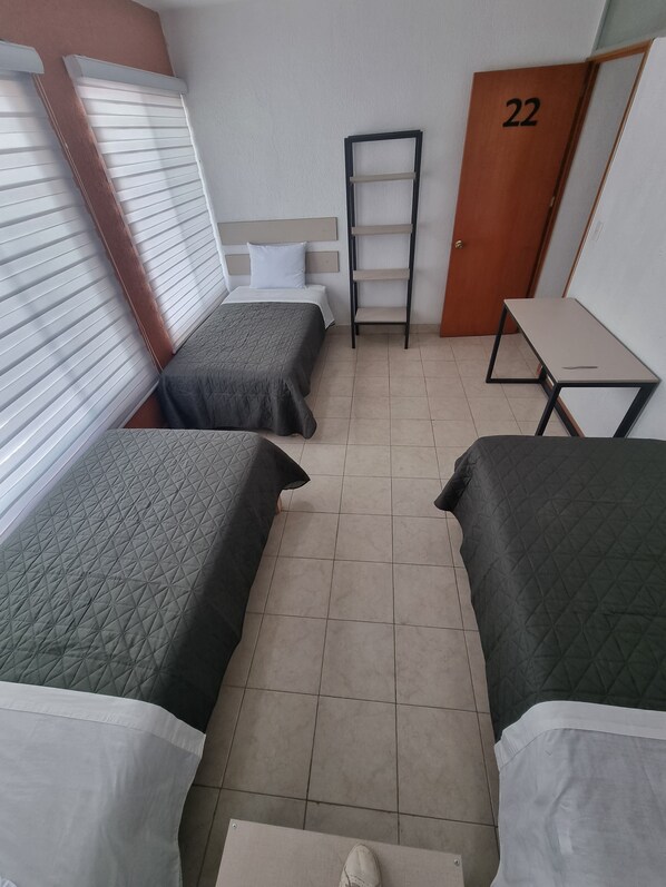 A small, compact room with two beds, a wooden door labeled '22', a small table, and a shelf.