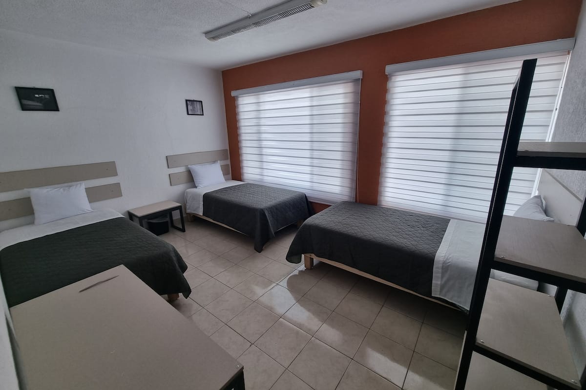 Quarto de hotel com duas camas de solteiro, uma escrivaninha e uma cama beliche.