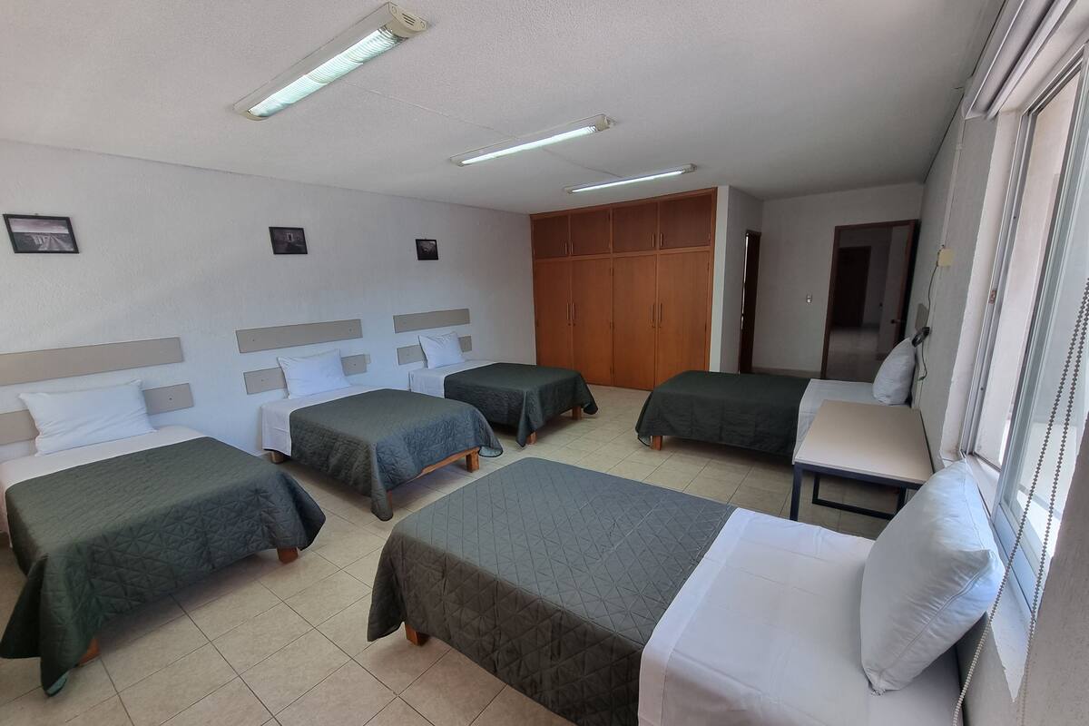Quarto de hotel com quatro camas, um guarda-roupa e uma janela.