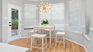 A dining area with a white table and four chairs, a potted plant, and a modern chandelier. - Incredible Heated Pool/HotTub! Gameroom-Movieroom! (Pflugerville)
