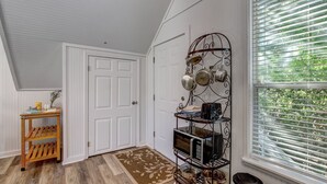 Une pièce avec une porte blanche, une étagère en bois sur laquelle est posé un tapis, et un présentoir en métal contenant des appareils de cuisine.