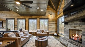 A cozy log cabin interior with a stone fireplace, leather sofas, and a round coffee table. - Game Room, Hot Tub, Fire Pit, Pets, High Horse (Broken Bow)