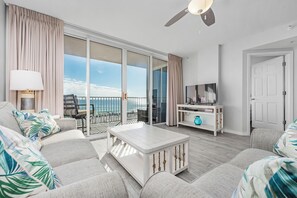 Una sala de estar con sofá, una mesa de centro, televisor y un balcón con vistas.