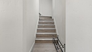 Un escalier étroit aux murs blancs, avec des marches en bois et une main courante en métal.