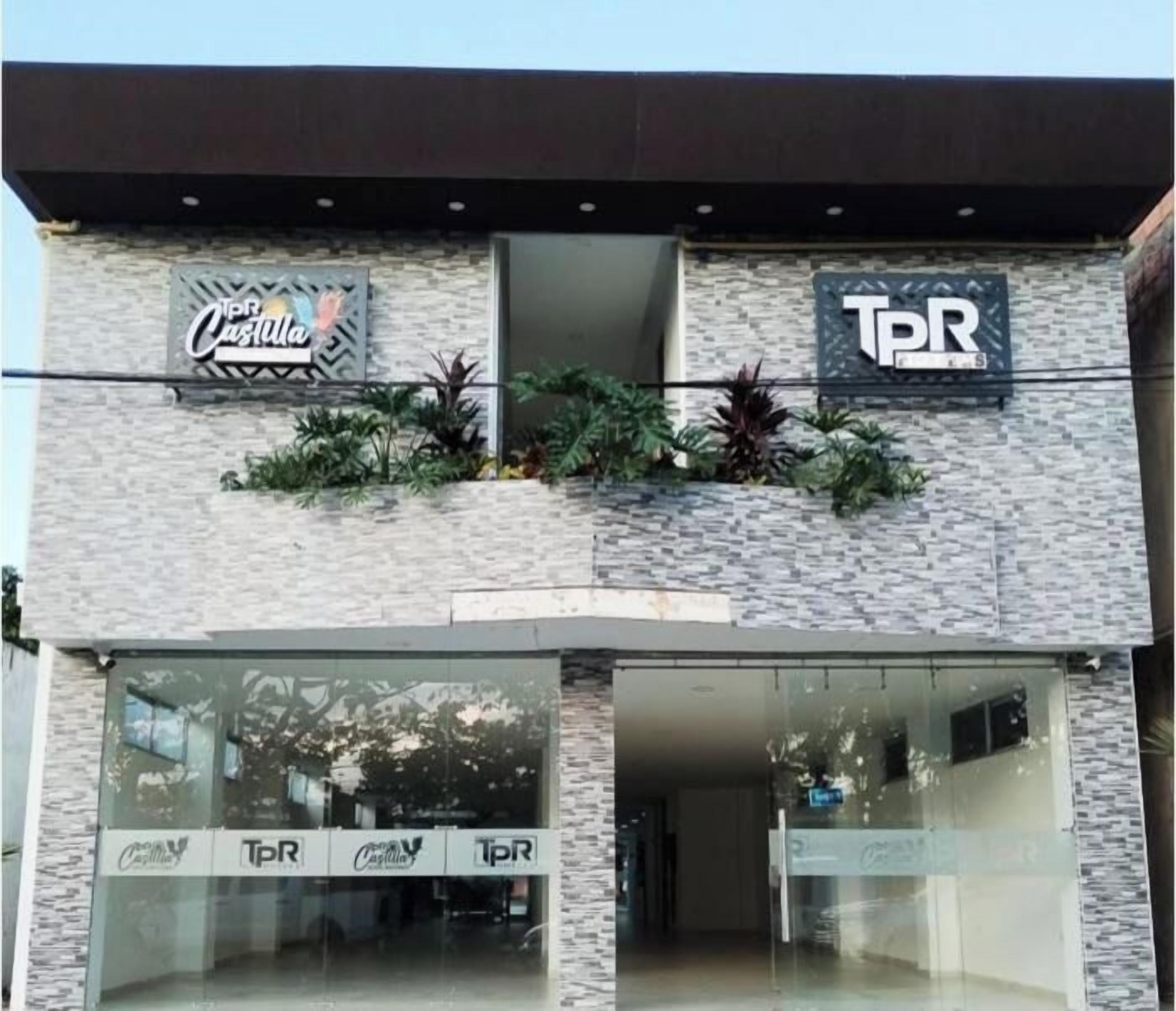 Fachada de un edificio con letreros de 'Coca-Cola' y 'TPR' en el nivel superior, y puertas de vidrio en el nivel inferior.
