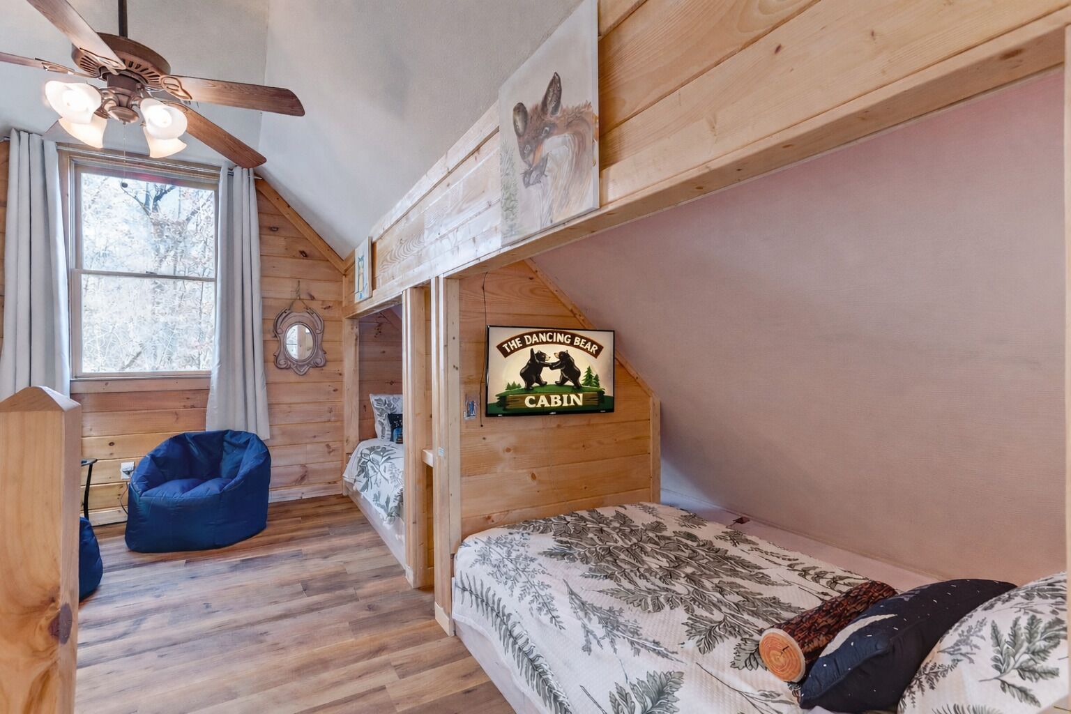 L’intérieur d’un chalet avec un lit en mezzanine, un fauteuil en forme de poire bleu, un ventilateur de plafond et une pancarte indiquant : « Le chalet de l’ours danseur ».