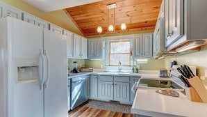 Una cocina con armarios blancos, techo de madera, lavavajillas integrado y un ventanal.