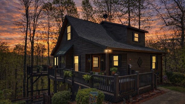 Una cabaña de madera con terraza, rodeada de árboles, al atardecer.