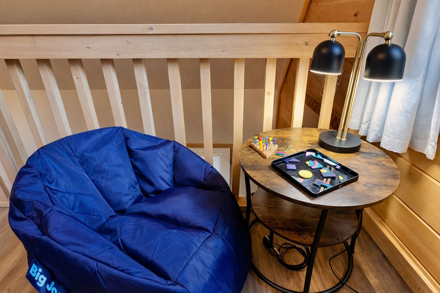 A cozy room with a blue bean bag chair, a small wooden table with a lamp, and a tray of colorful shapes.