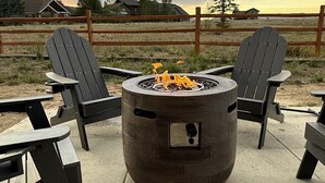 Ein Feuerkorb mit zwei Adirondack-Stühlen und einem Tisch, umgeben von einer Beton-Terrasse.