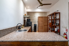 A kitchen with granite countertops, a built-in sink, a stove, a microwave, and a wooden shelving unit with dishes.