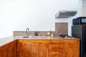 A kitchen with a granite countertop, wooden cabinets, a stainless steel sink, a gas stove, and a black refrigerator.
