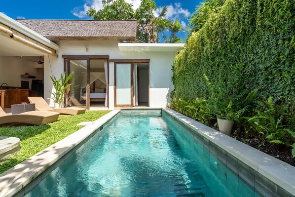 A swimming pool with a clear blue water surface, surrounded by a well-maintained lawn and a hedge.