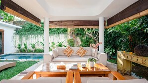 Un espacio exterior moderno con un sofá blanco, una mesa de centro de madera y cojines.