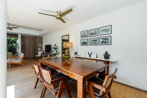 Un comedor con una mesa y sillas de madera, un ventilador de techo y cuadros en la pared.