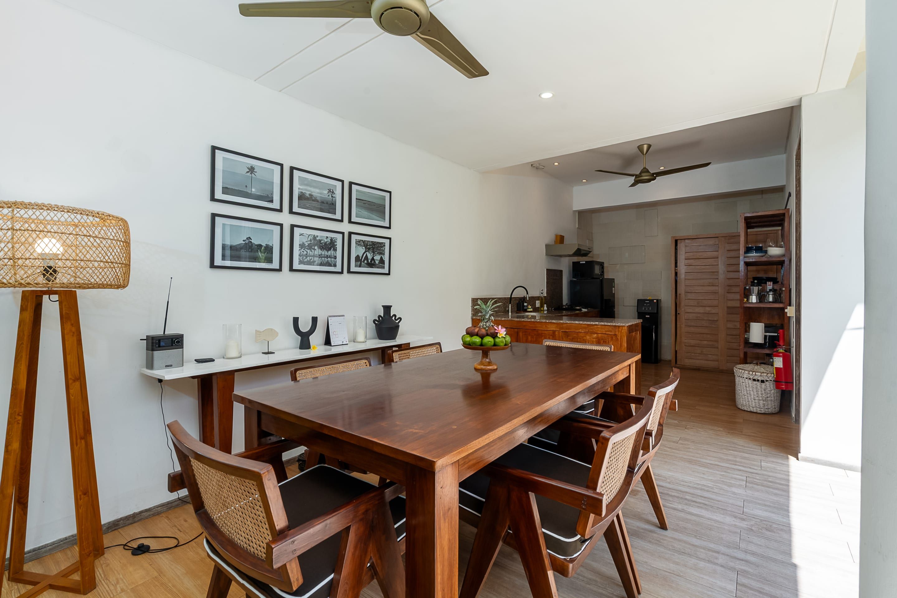 A dining area with a wooden table and chairs, a ceiling fan, and framed pictures on the wall.